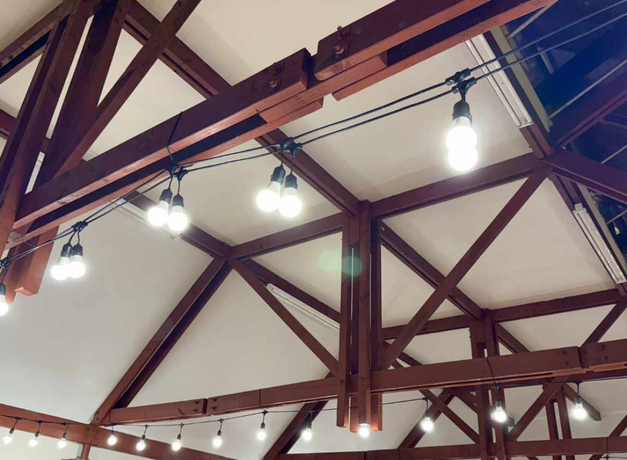 An Auckland venue ceiling with exposed wooden beams and warm festoon lighting, expertly styled by Light and Leaf Co.