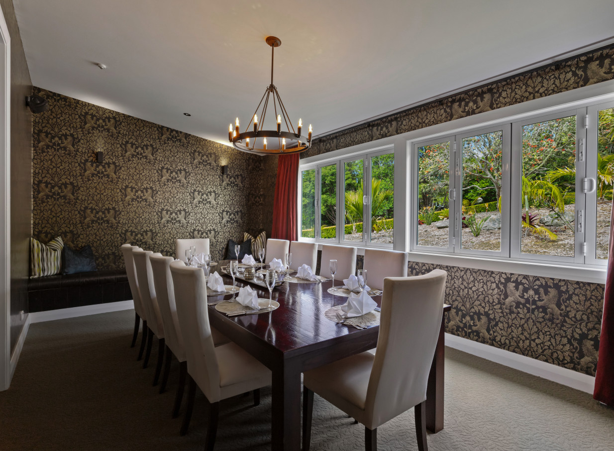 A stylish lodge-style private dining room at Woodhouse Mountain Lodge, Auckland, offers serene views of lush gardens.