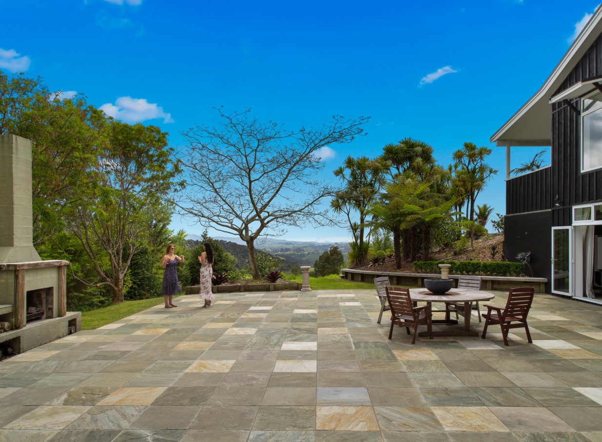 The contemporary outdoor patio at Woodhouse Mountain Lodge, Auckland, features a fireplace, dining area, and stunning mountain views.