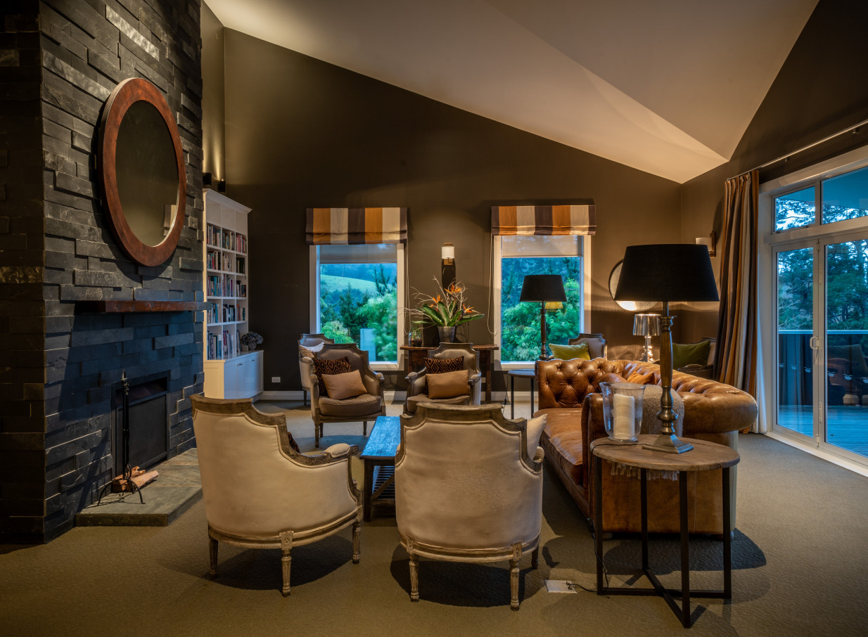 The cozy and elegant lounge at Woodhouse Mountain Lodge, Auckland, features classic furnishings by a prominent stone fireplace.