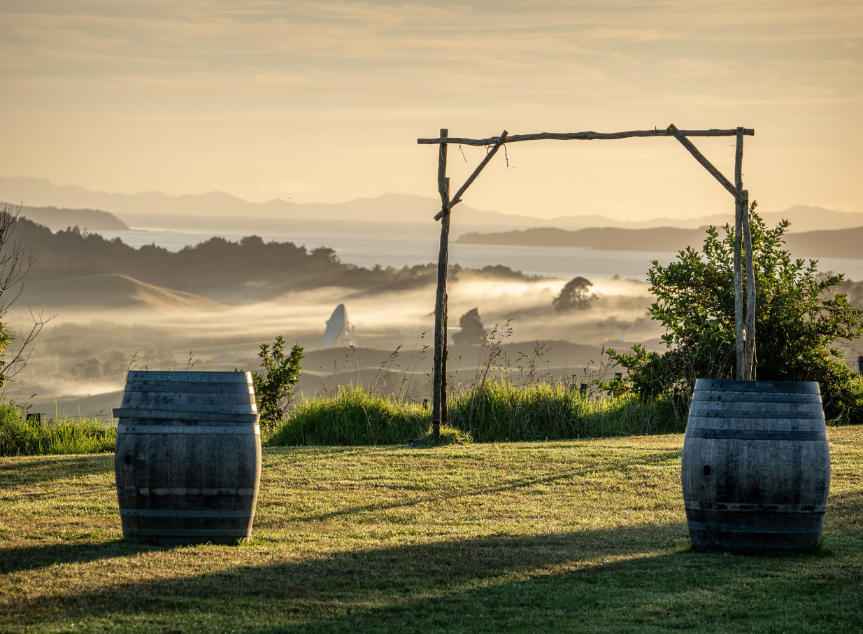 An outdoor ceremony arch and barrels at the elegant Woodhouse Mountain Lodge in Auckland, overlooking a stunning misty Hauraki Gulf view.
