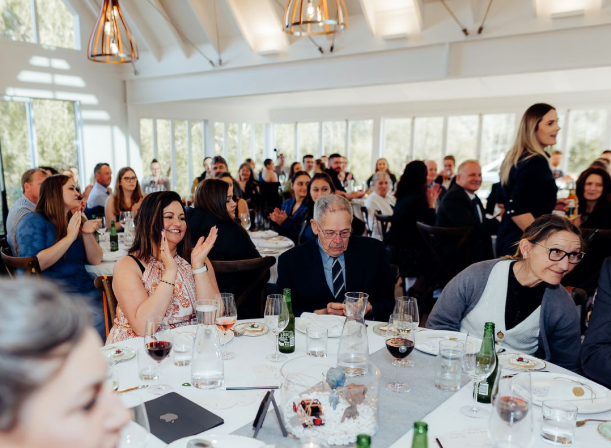 Guests clap during a reception at Abel Estate Auckland's modern winery-style venue, featuring high vaulted ceilings and large windows.