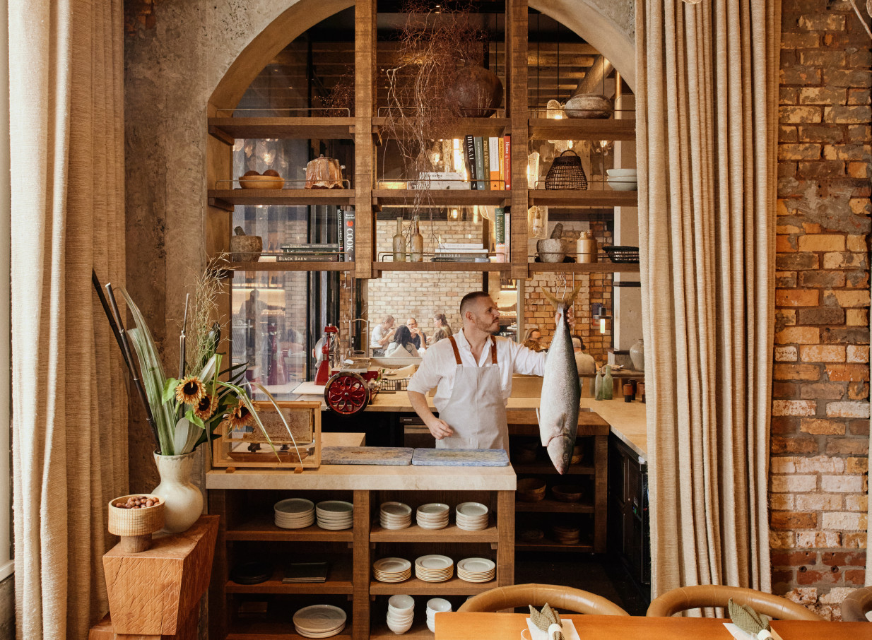A chef presents fresh fish in the industrial-chic kitchen of Kingi at The Hotel Britomart, Auckland, renowned for its sustainable seafood.