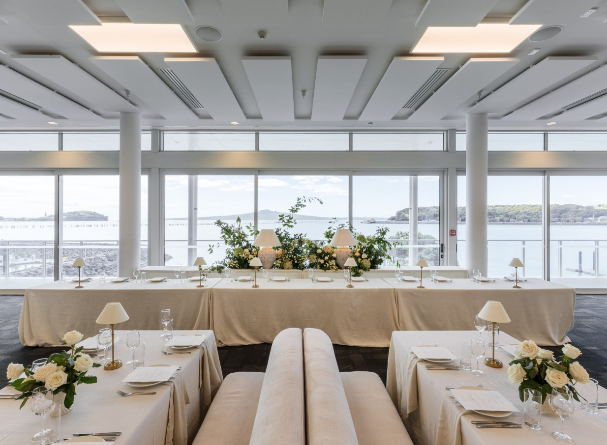An elegant dining room setup at Akarana Event Centre, Auckland, offering panoramic waterfront views.