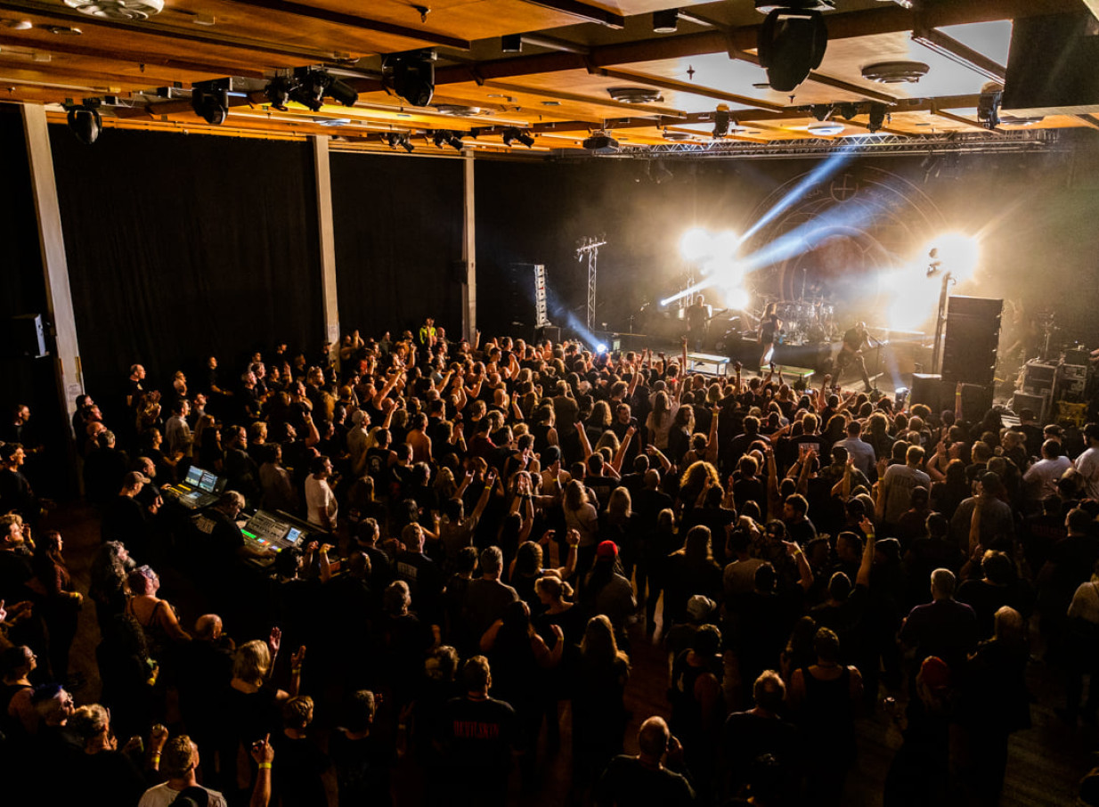 A vibrant concert crowd fills Forum North's Whangarei performance space, featuring a distinctive timber-lined ceiling.