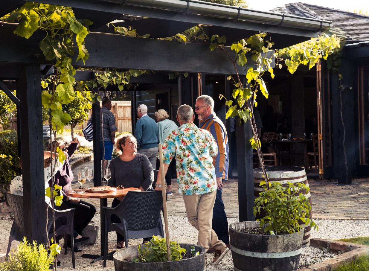 An outdoor dining area under a vine-covered pergola at Omata Estate, a rustic boutique vineyard in the Bay of Islands.