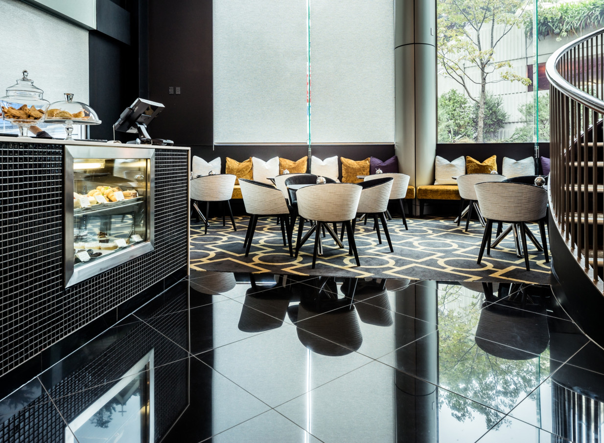This modern, elegant lobby café at Bolton Hotel in Wellington showcases sophisticated black and gold decor with comfortable seating and pastries.
