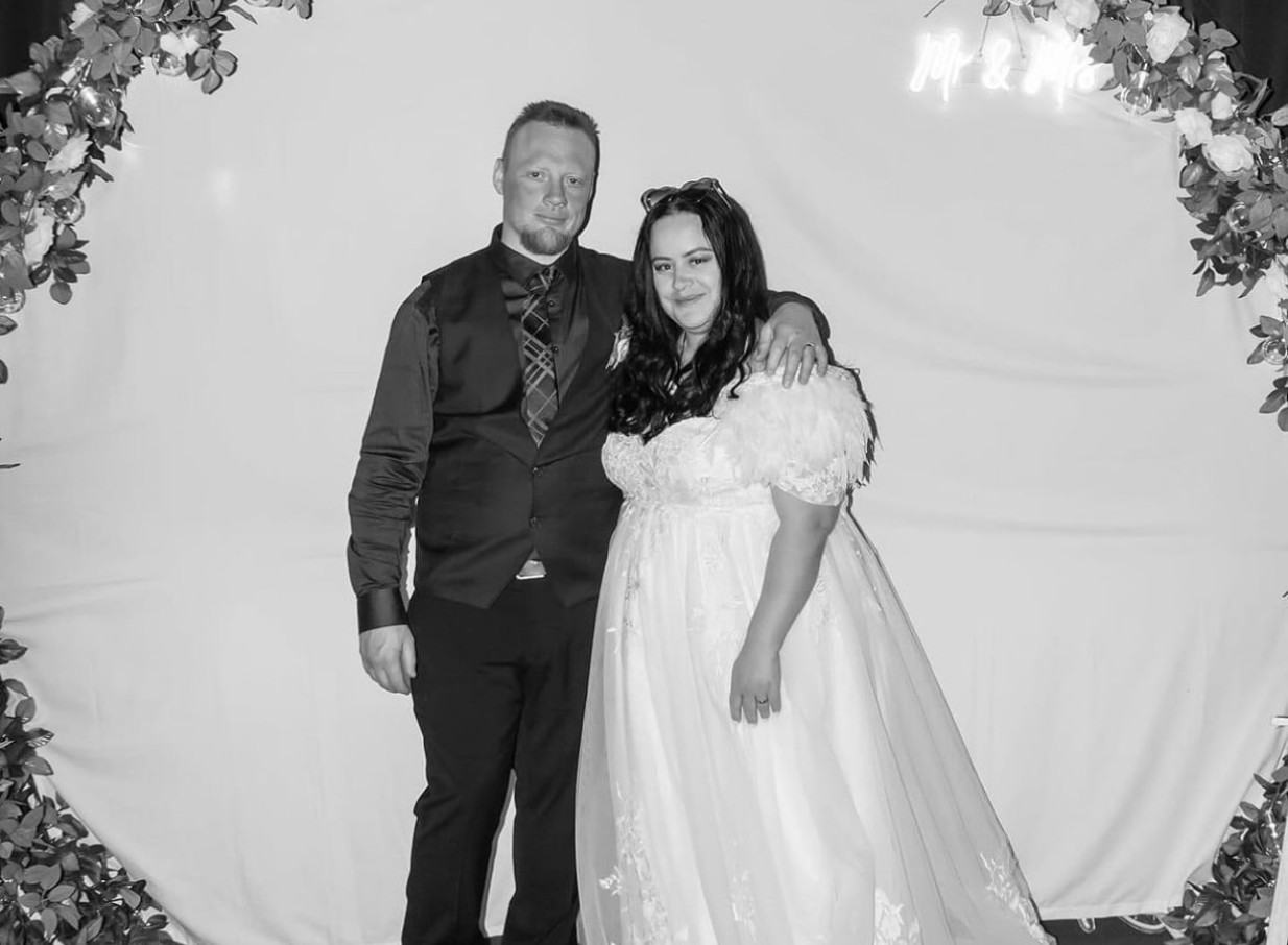 A newlywed couple poses in a customisable event space at Westend, Christchurch, featuring a floral arch and "Mr & Mrs" neon sign.