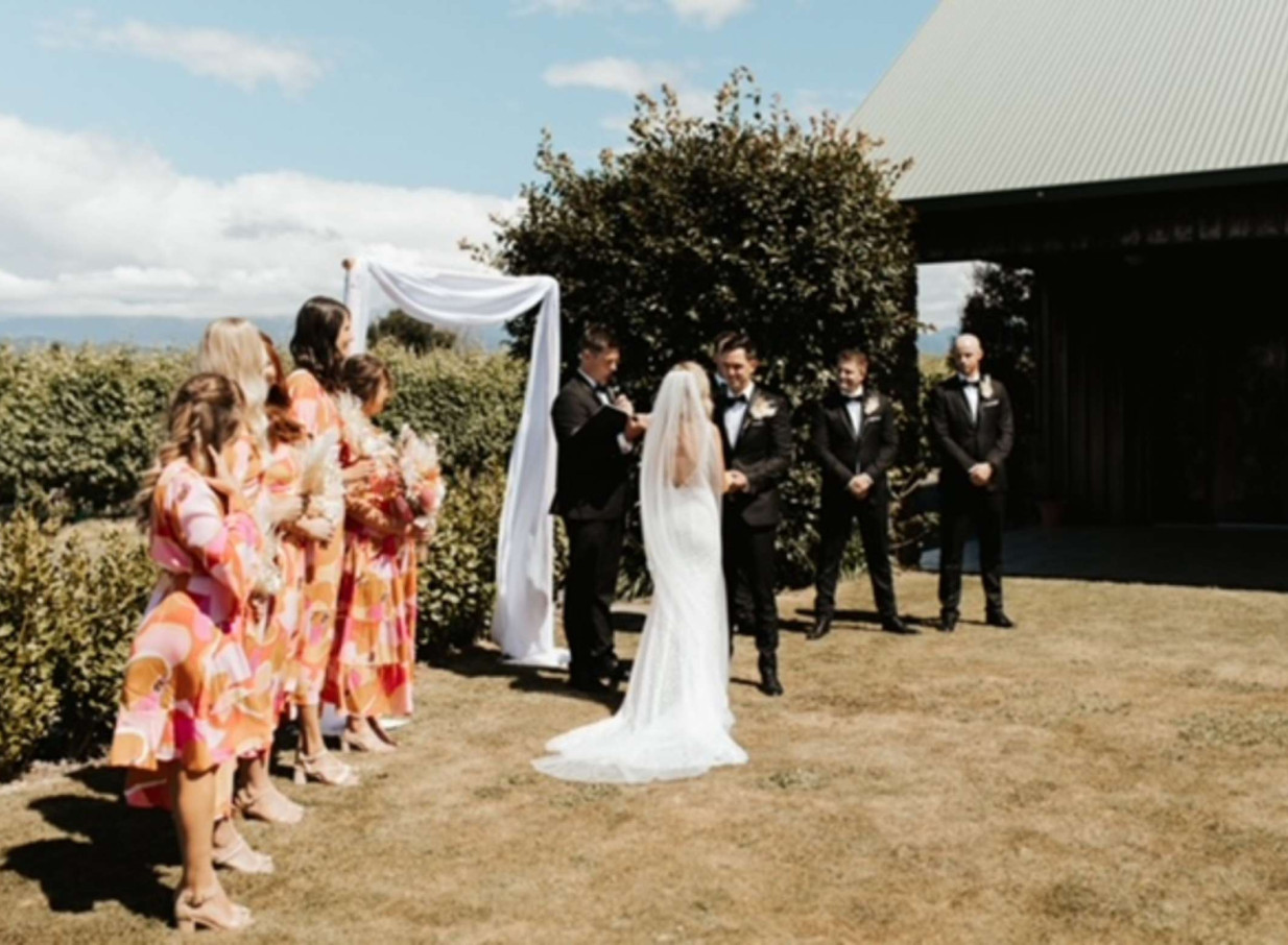 An outdoor wedding ceremony takes place on the lawn at the rustic Harvest Kitchen, a vineyard venue in Nelson-Tasman.
