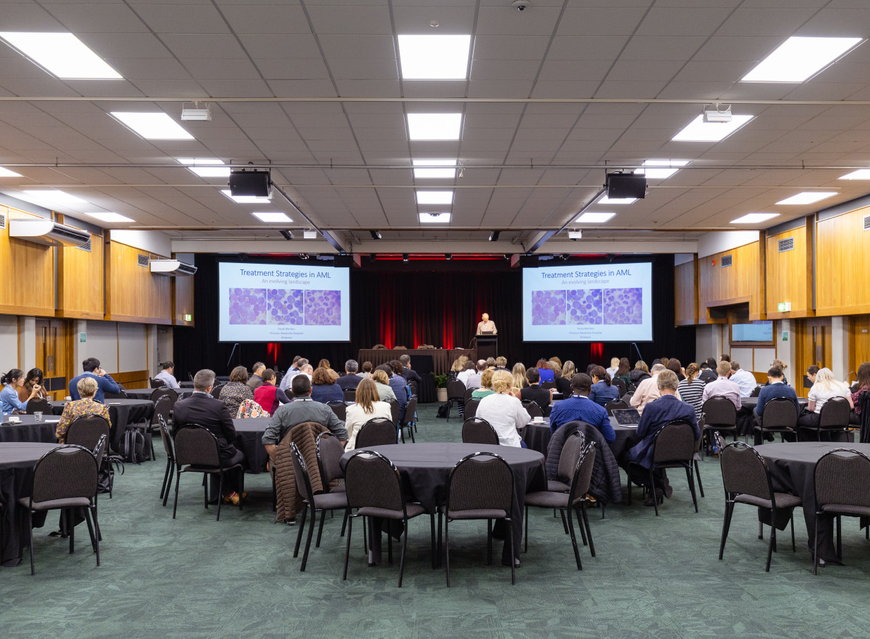 A large conference presentation at the modern Palmy Conference + Function Centre in Palmerston North, featuring dual screens and round tables.