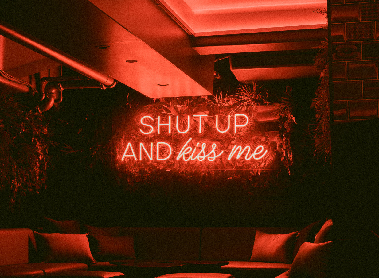 Auckland's Cellar Bar, a chic, dimly lit underground lounge, features a vibrant red "Shut up and Kiss me" neon sign.