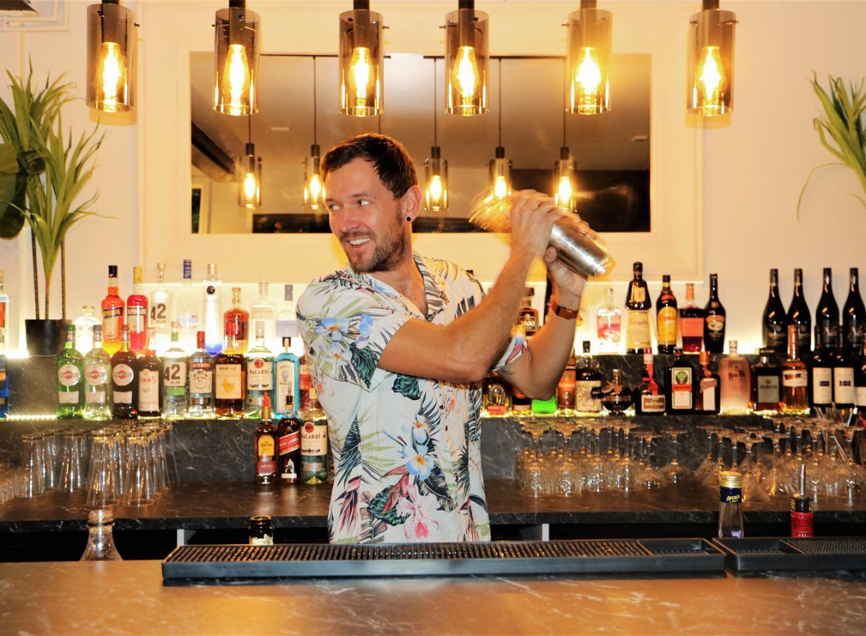 A bartender crafts a cocktail at Rosanna's Garden Bar, an urban oasis in Auckland, under modern pendant lights.