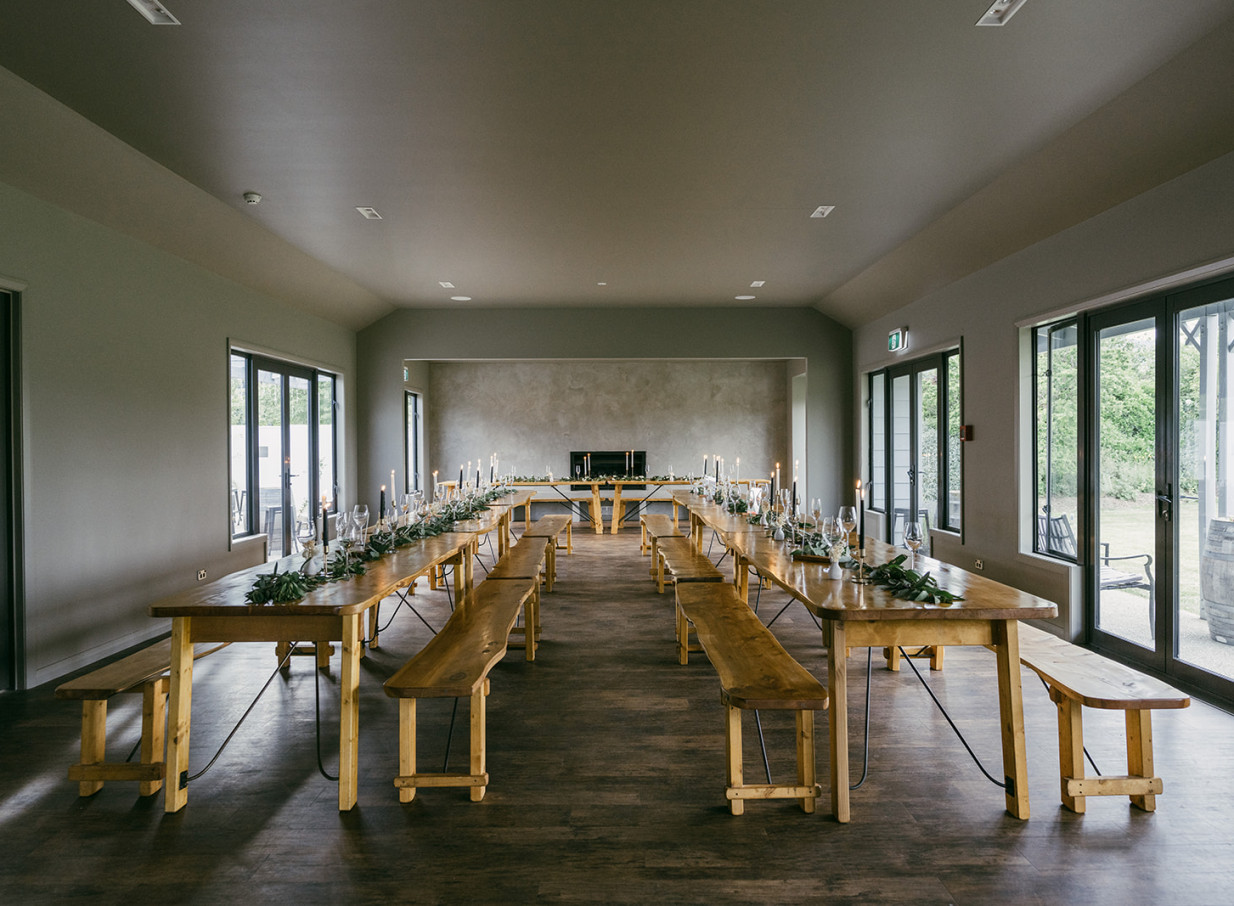 The Venue Wānaka presents a rustic-chic dining room with long wooden tables and benches, elegantly set for a special event.