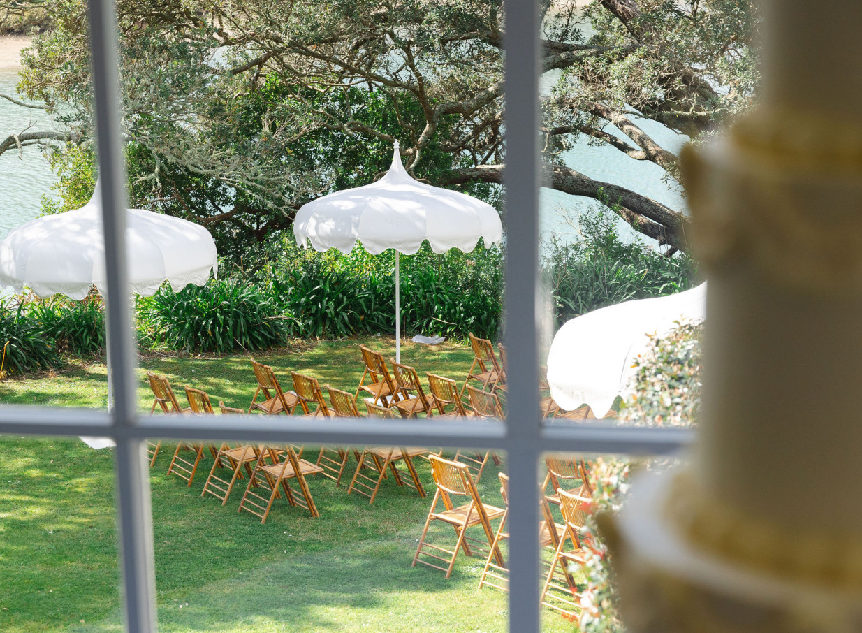 Outdoor ceremony with white umbrellas on a grassy lawn at Orakei Bay, Auckland's iconic waterside event venue.