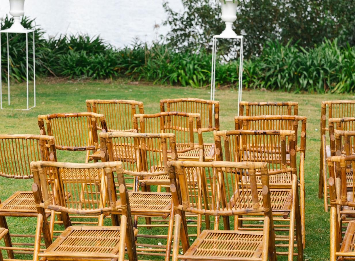 Rows of natural bamboo chairs arranged on a grassy lawn for an outdoor ceremony at the waterside Orakei Bay venue in Auckland.
