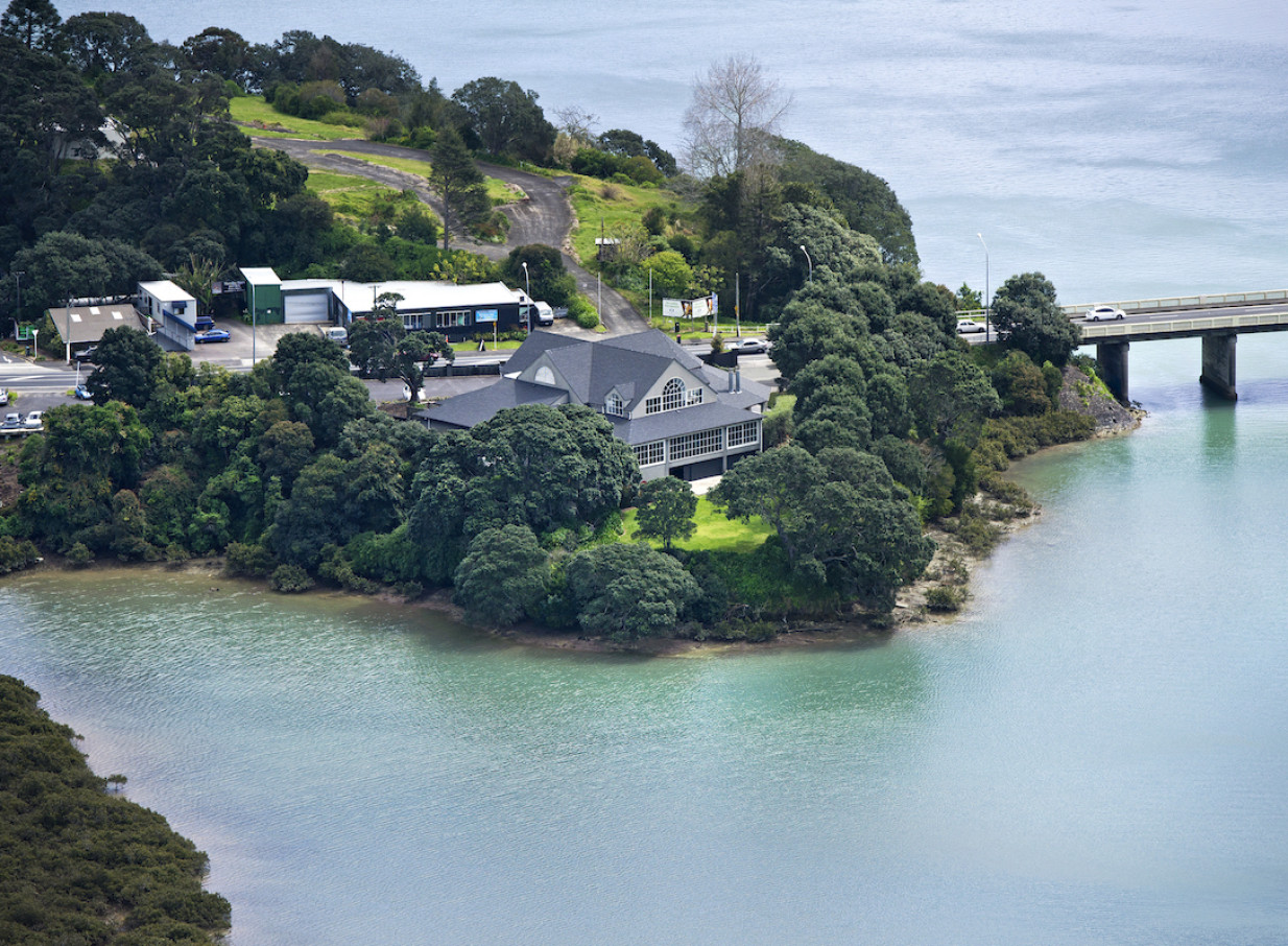 An aerial view of the elegant multi-level Orakei Bay venue in Auckland, nestled by lush trees with stunning water views.