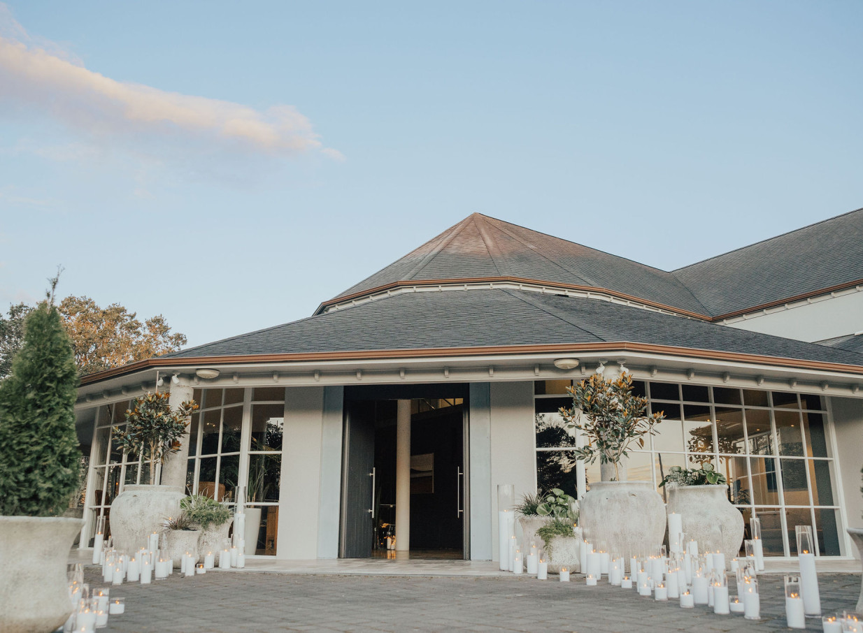 An inviting entrance to the modern waterside event venue, Orakei Bay Auckland, illuminated by candles and featuring large windows.