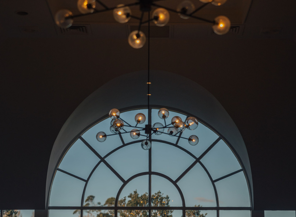 A modern chandelier illuminates the elegant arched window of Orakei Bay, Auckland's waterside venue.