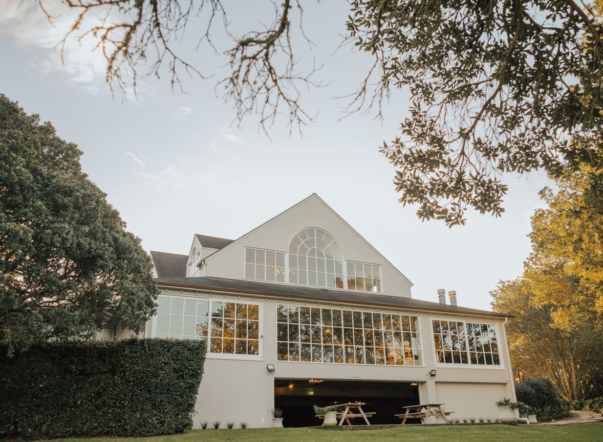 Exterior view of the modern and elegant Orakei Bay event venue in Auckland, featuring large windows and surrounding greenery.