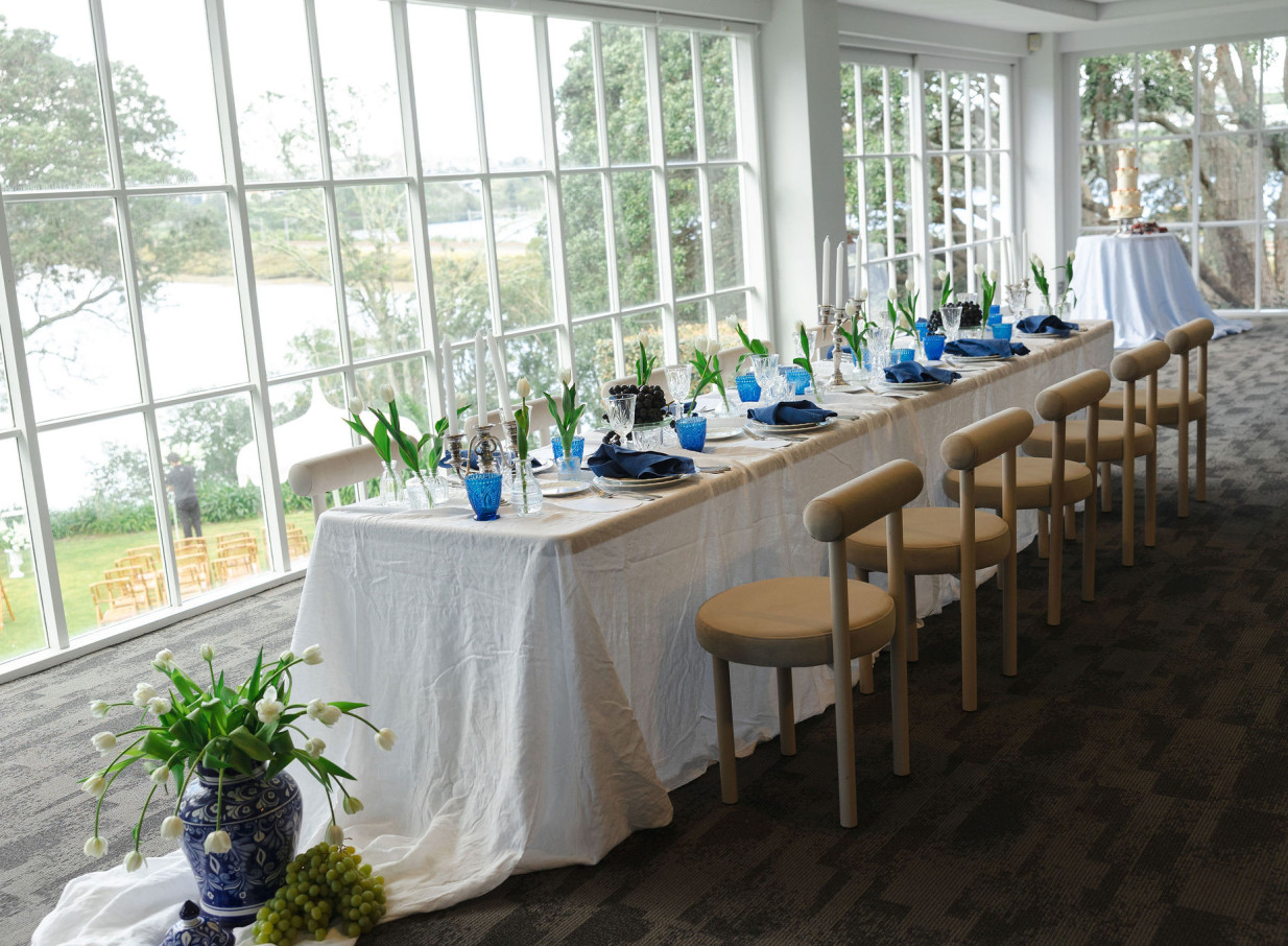 An elegant dining setup at Orakei Bay, Auckland, showcasing waterside views through its expansive, floor-to-ceiling windows.