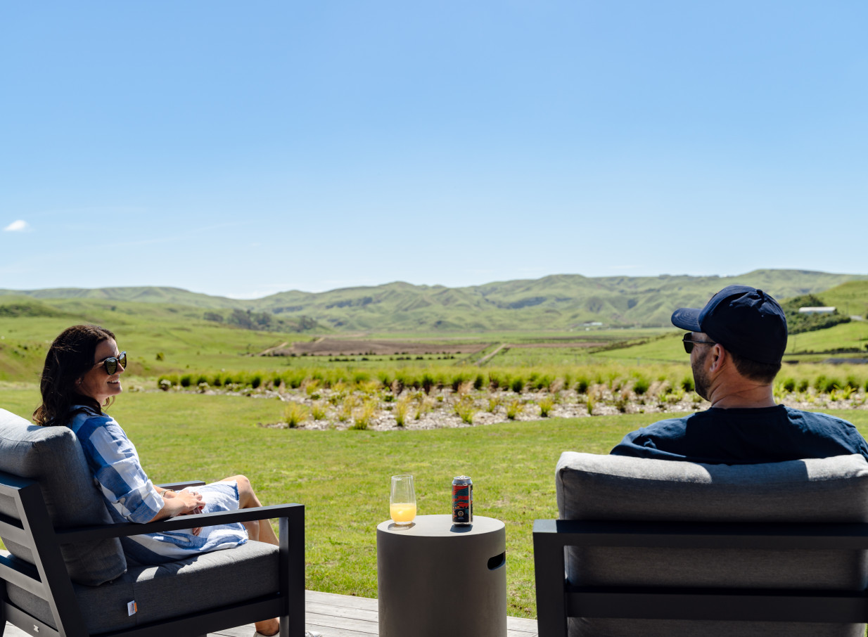 A couple enjoys the breathtaking rural landscape from the veranda of the contemporary Te Karaka Lodge in Waikato.