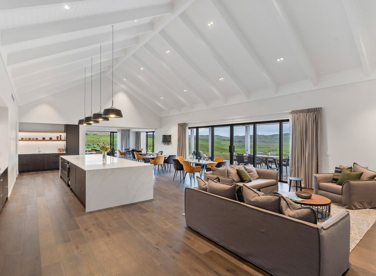 A modern farmstay living and dining area at Te Karaka Lodge, Waikato, features vaulted ceilings and scenic rural views.