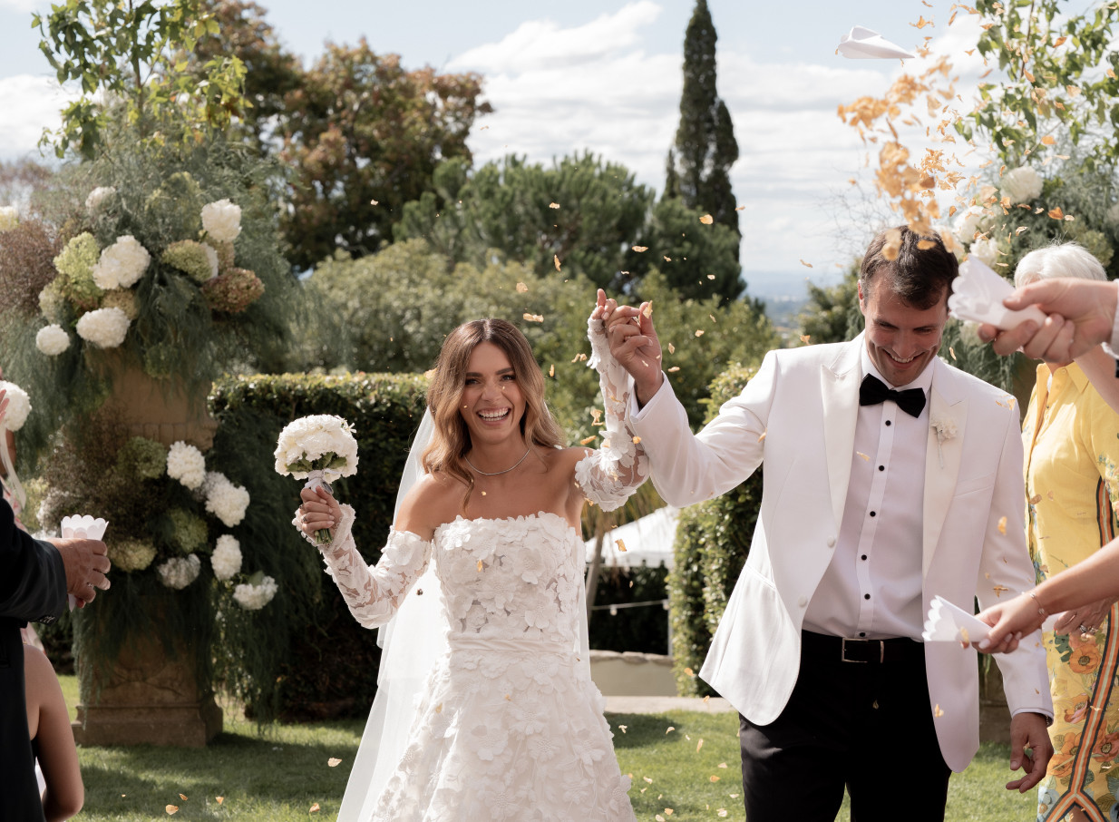 A smiling couple celebrates their outdoor wedding with confetti at the 1920s Mediterranean-style Kōtare Estate in Hawke's Bay.