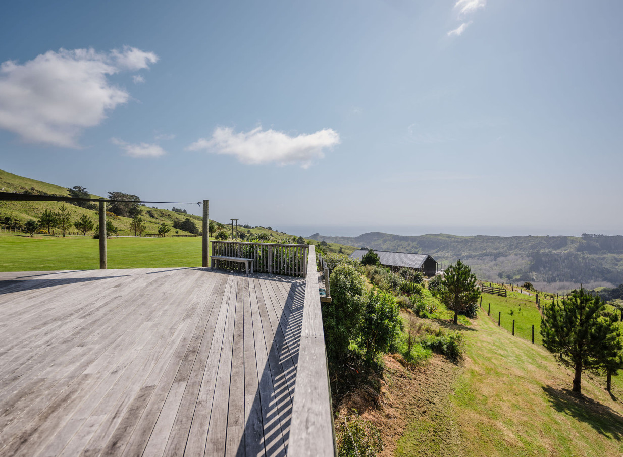 The rustic wooden deck at Vanderosa Farms in Auckland offers panoramic views of rolling hills and the Pacific Ocean.