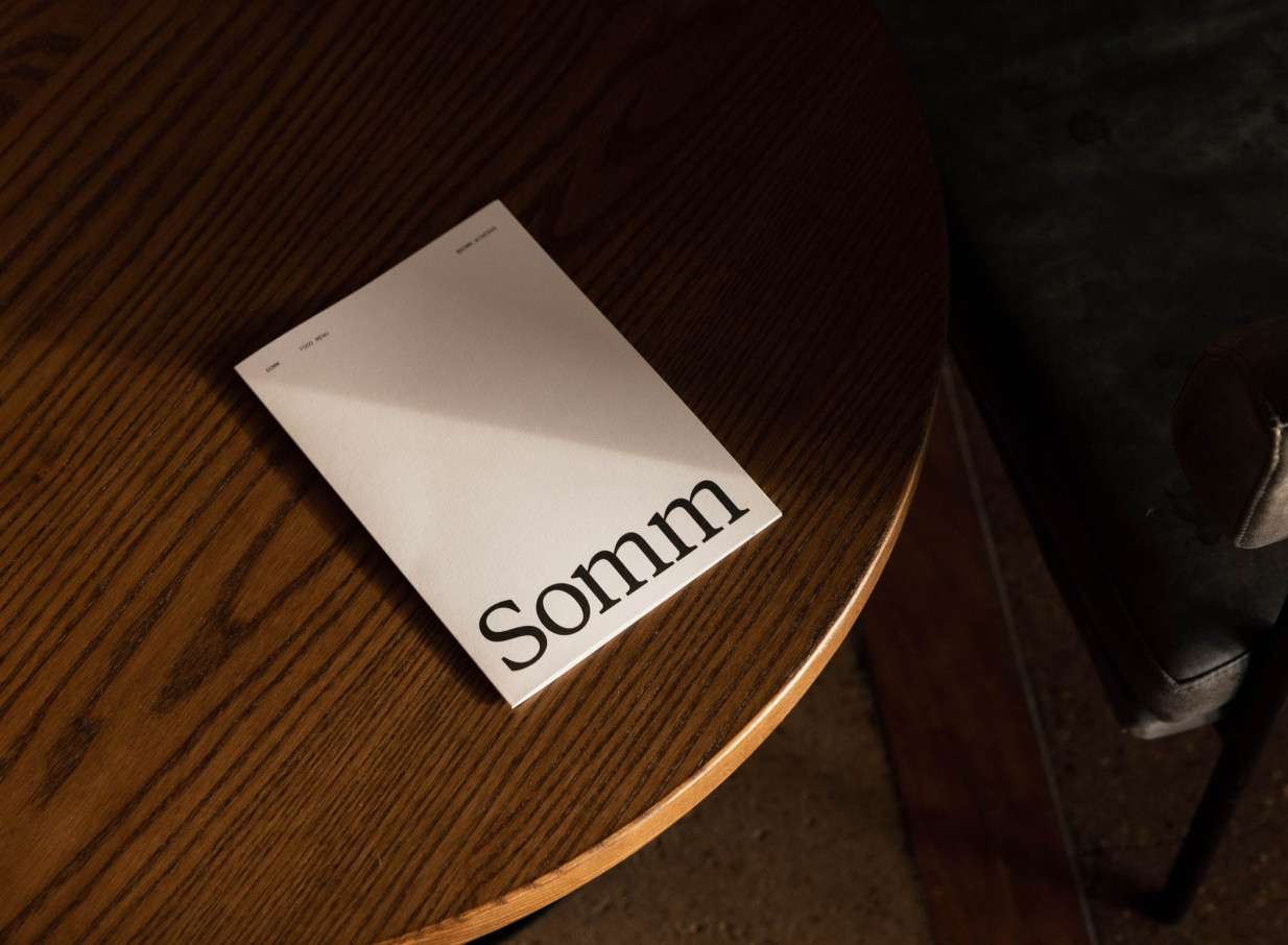 A menu for Somm, Auckland's chic urban cellar door and wine bar, rests on a warm oak timber table.