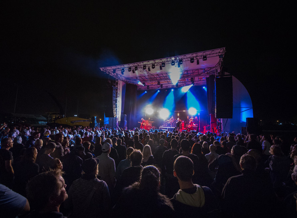 An outdoor concert featuring a band on a brightly lit stage in the modern, multi-purpose Central Energy Trust Arena in Palmerston North, with a large crowd gathered.