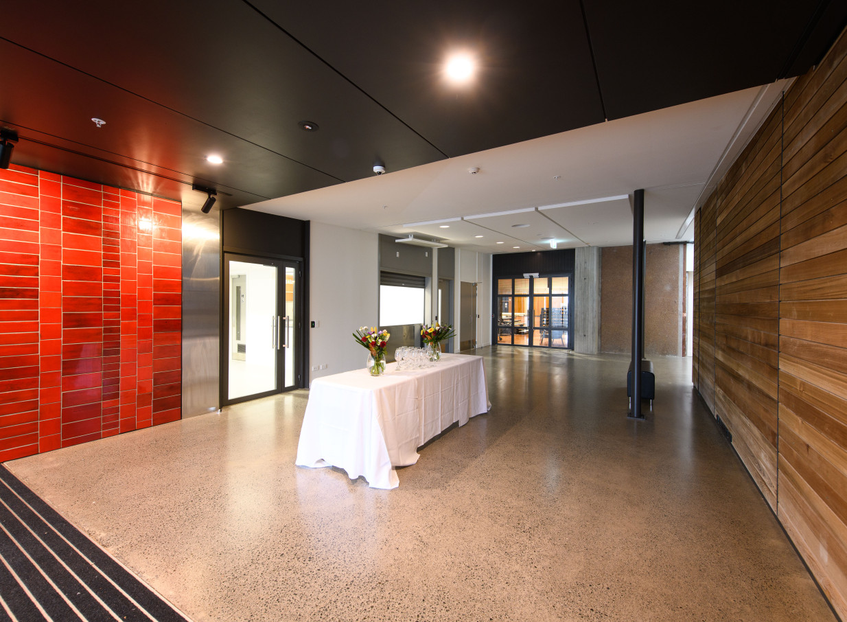 A modern event foyer at Whirinaki Whare Taonga, Wellington, featuring a table with flowers and contemporary red-tiled and wooden walls.