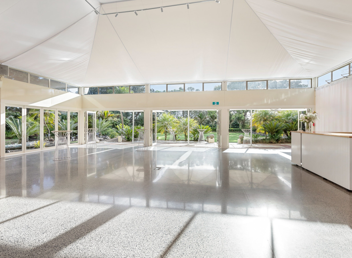 The luxurious white Pavilion event space at Puketutu Island Estate in Auckland, overlooking lush gardens.