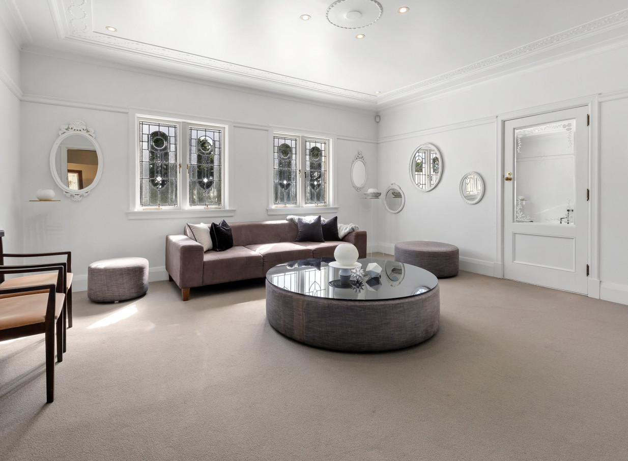 An elegant Spanish Mission-style lounge at Puketutu Island Estate, Auckland, featuring bright white walls and stained-glass windows.