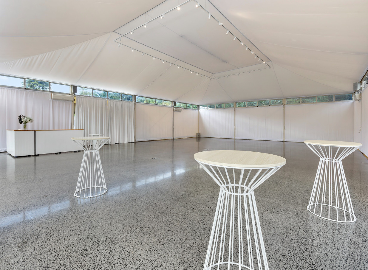 A bright, modern Pavilion event space with a bar and cocktail tables at the Spanish Mission-style Puketutu Island Estate, Auckland.