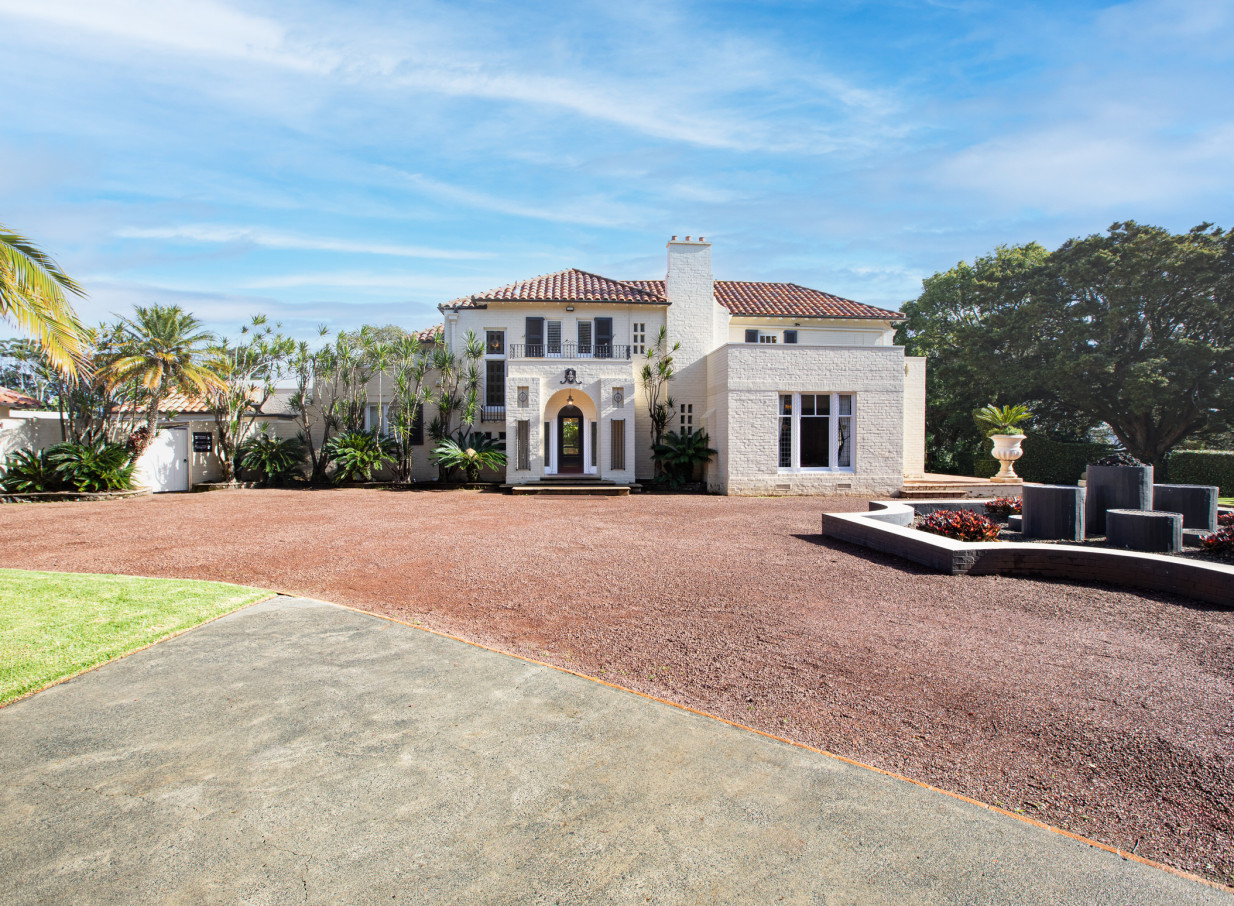 An exterior view of the Spanish Mission-style Puketutu Island Estate in Auckland, featuring a grand entrance and gravel driveway.