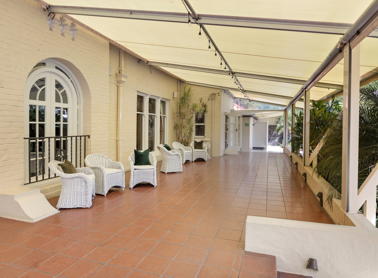 Puketutu Island Estate, Auckland, features a covered Spanish Mission-style patio with white wicker seating and terracotta tiles.