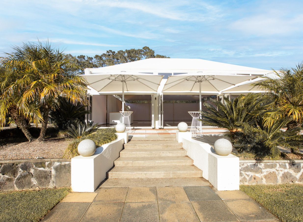 The elegant white pavilion at Puketutu Island Estate, Auckland, nestled within lush tropical gardens, ready for events.