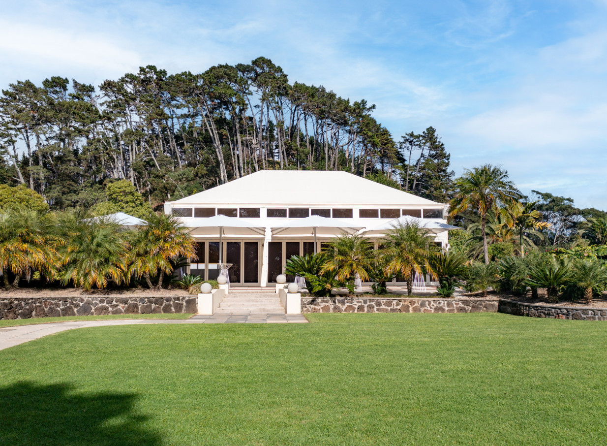 A luxurious white event pavilion overlooks a sprawling green lawn at Puketutu Island Estate in Auckland.