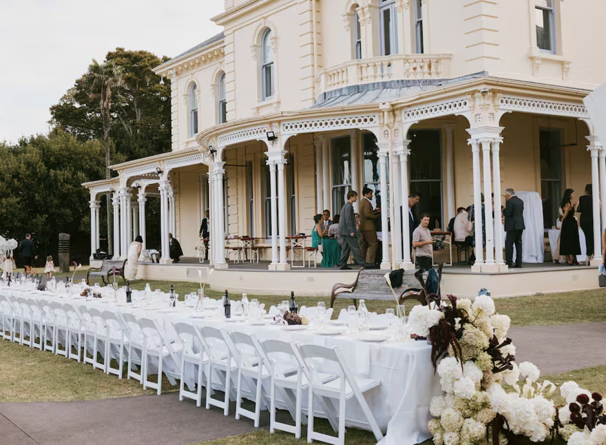 An outdoor reception setup graces the lawn of the Italianate Pah Homestead in Auckland, with guests on its wide verandah.