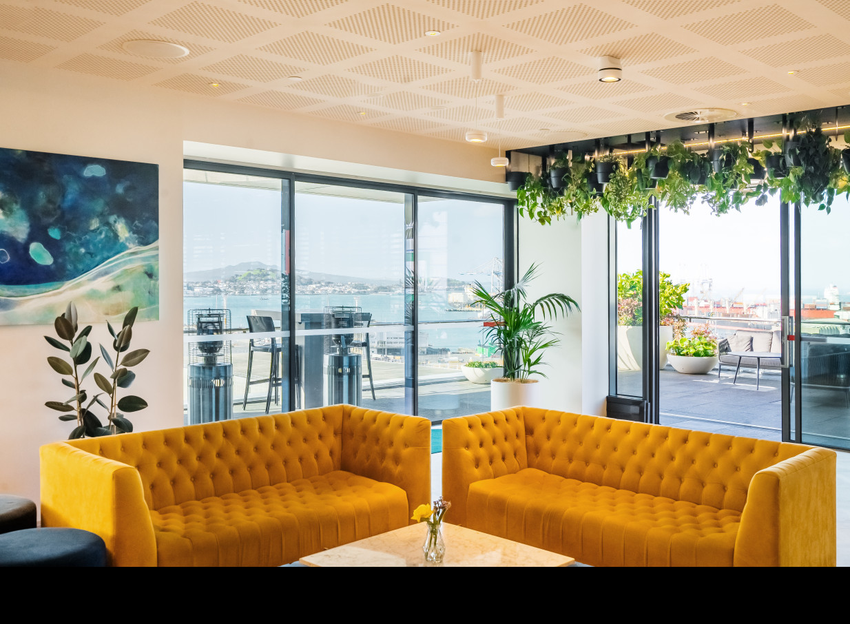 A modern, sophisticated lounge with lush plants at Britomart Place by Precinct Flex, Auckland, offers stunning harbour views.