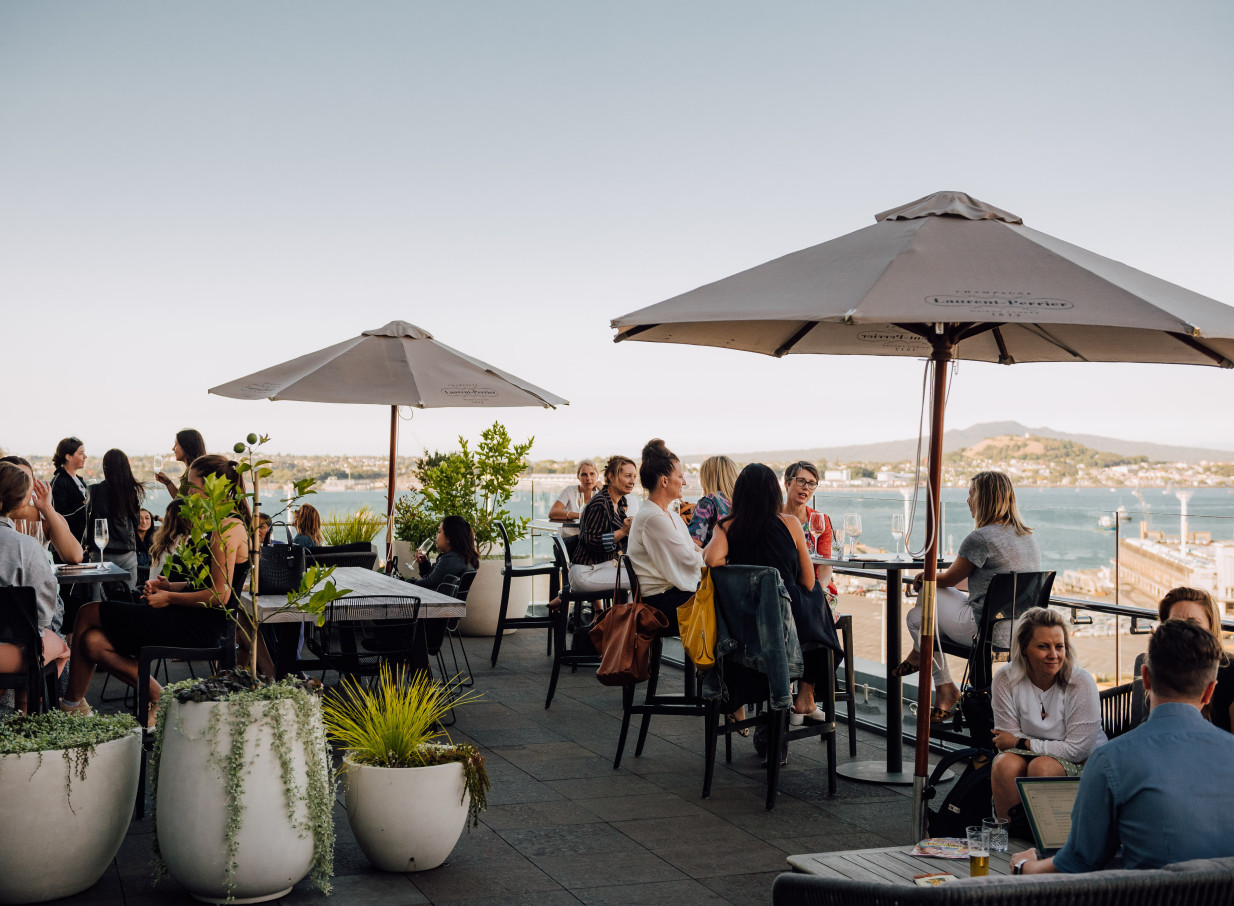 Guests gather at the stylish rooftop bar of Britomart Place by Precinct Flex in Auckland, enjoying harbor views.