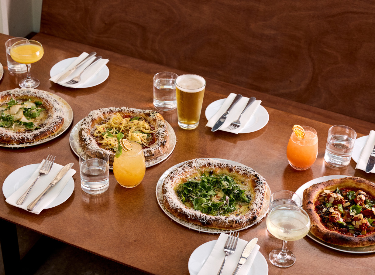 A dining scene featuring multiple Neapolitan pizzas and drinks on a wooden table in Norma Taps, Auckland's industrial-chic bar.