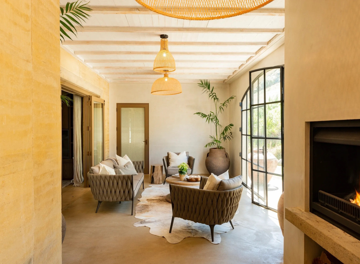 This Tuscan-inspired living area at Muriwai Estate in Auckland features cozy seating, a fireplace, and natural decor.