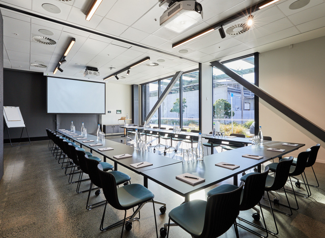 A modern, industrial-chic U-shaped meeting room with a projector screen at 12 Madden St by Precinct Flex in Auckland.