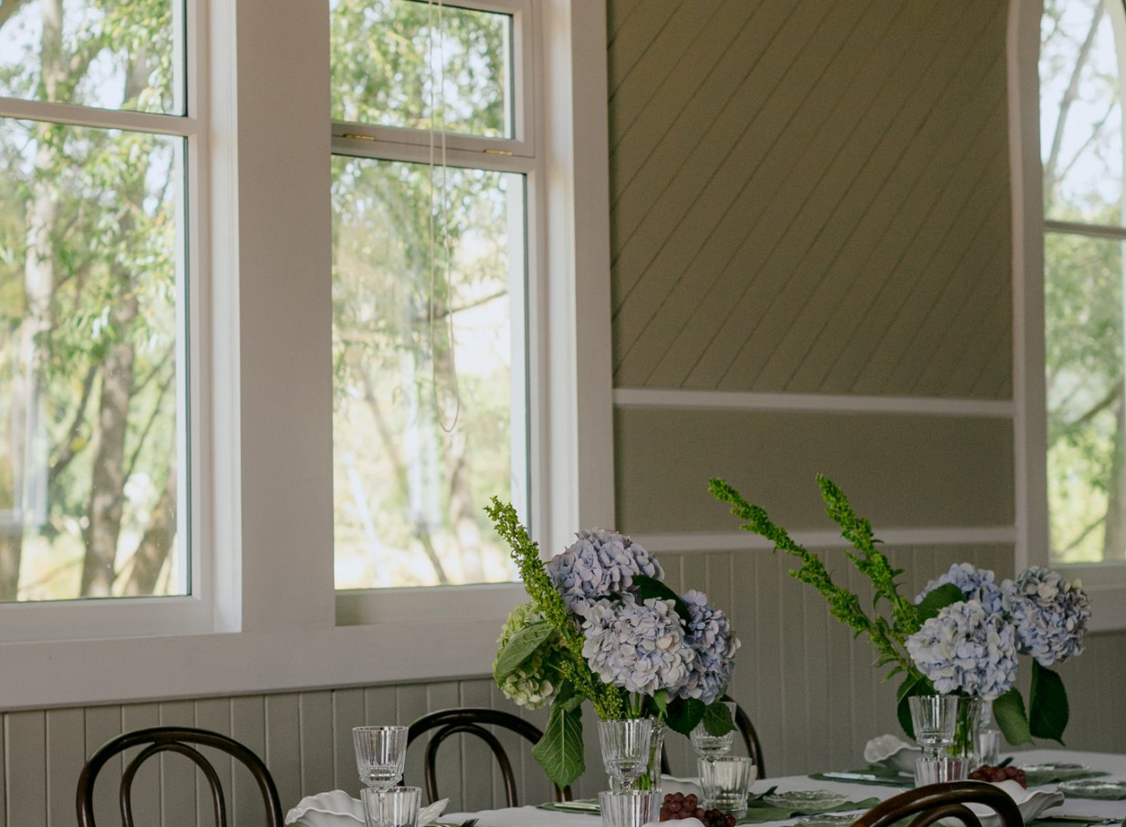 An elegantly set dining space with floral centerpieces in the bright, restored heritage interior of Waikākā Church, Queenstown.