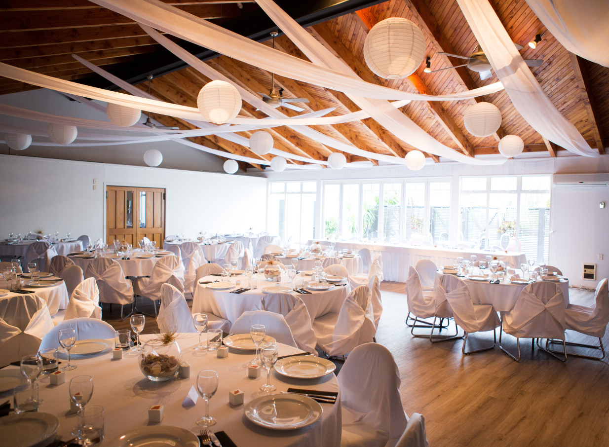 Taipa Beach Resort's Northland reception room features a warm A-frame ceiling, white drapes, and lanterns, ready for an event.