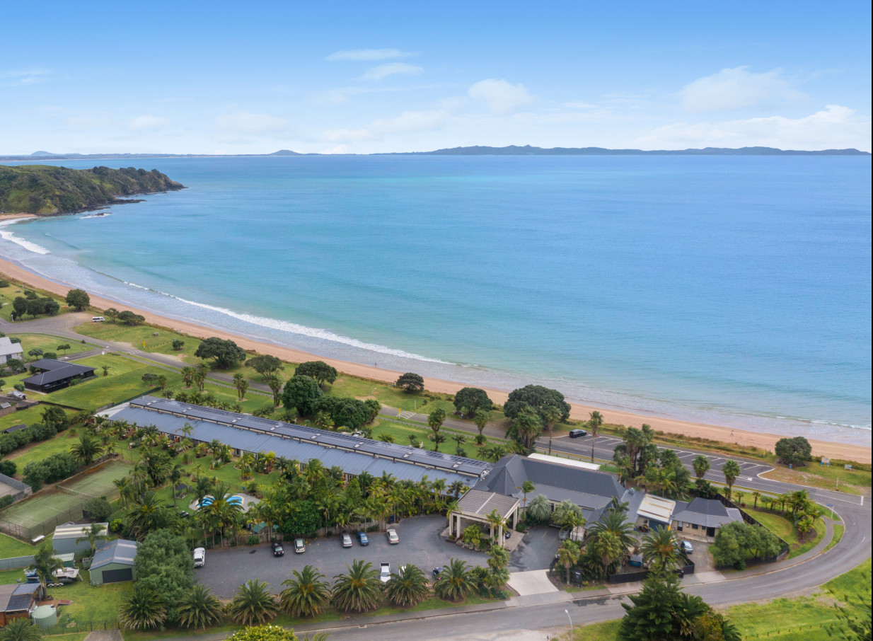 An aerial view of the modern, tropically landscaped Taipa Beach Resort in Northland, nestled along a sandy beach.