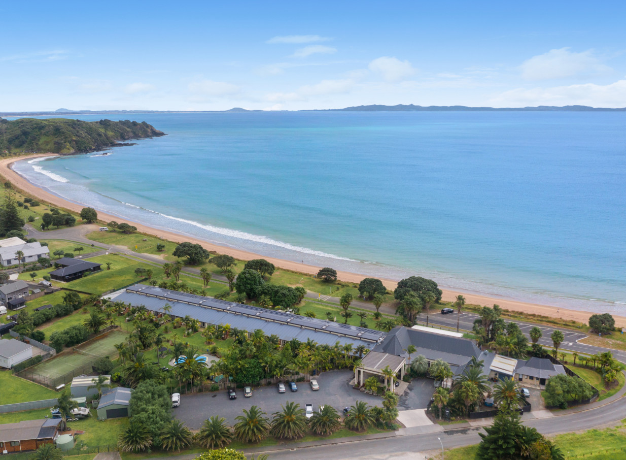 An aerial view of Taipa Beach Resort in Northland, featuring modern beachfront buildings, a tropical pool, and lush gardens.