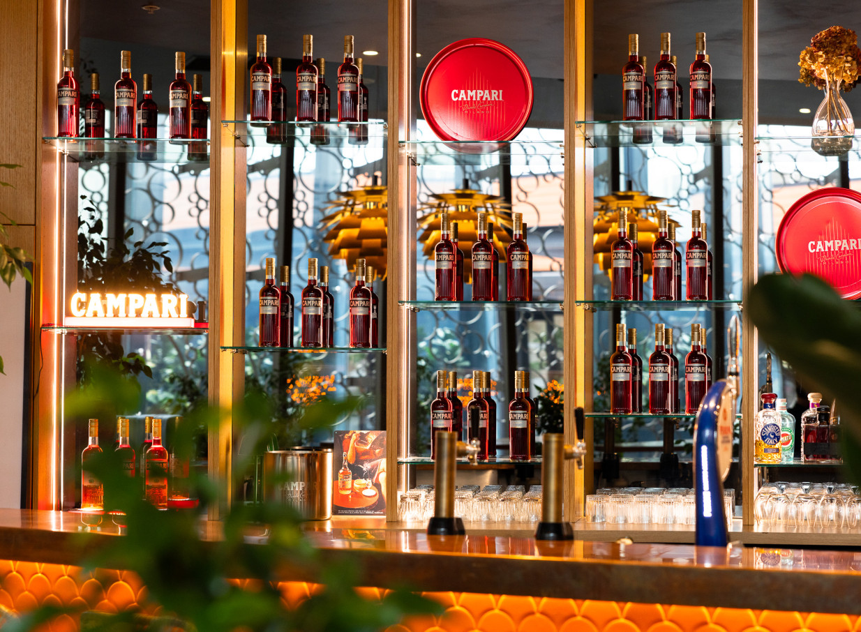 The vibrant, retro-inspired bar at Bar Franco in Christchurch, featuring shelves stocked with Campari bottles and a neon sign.
