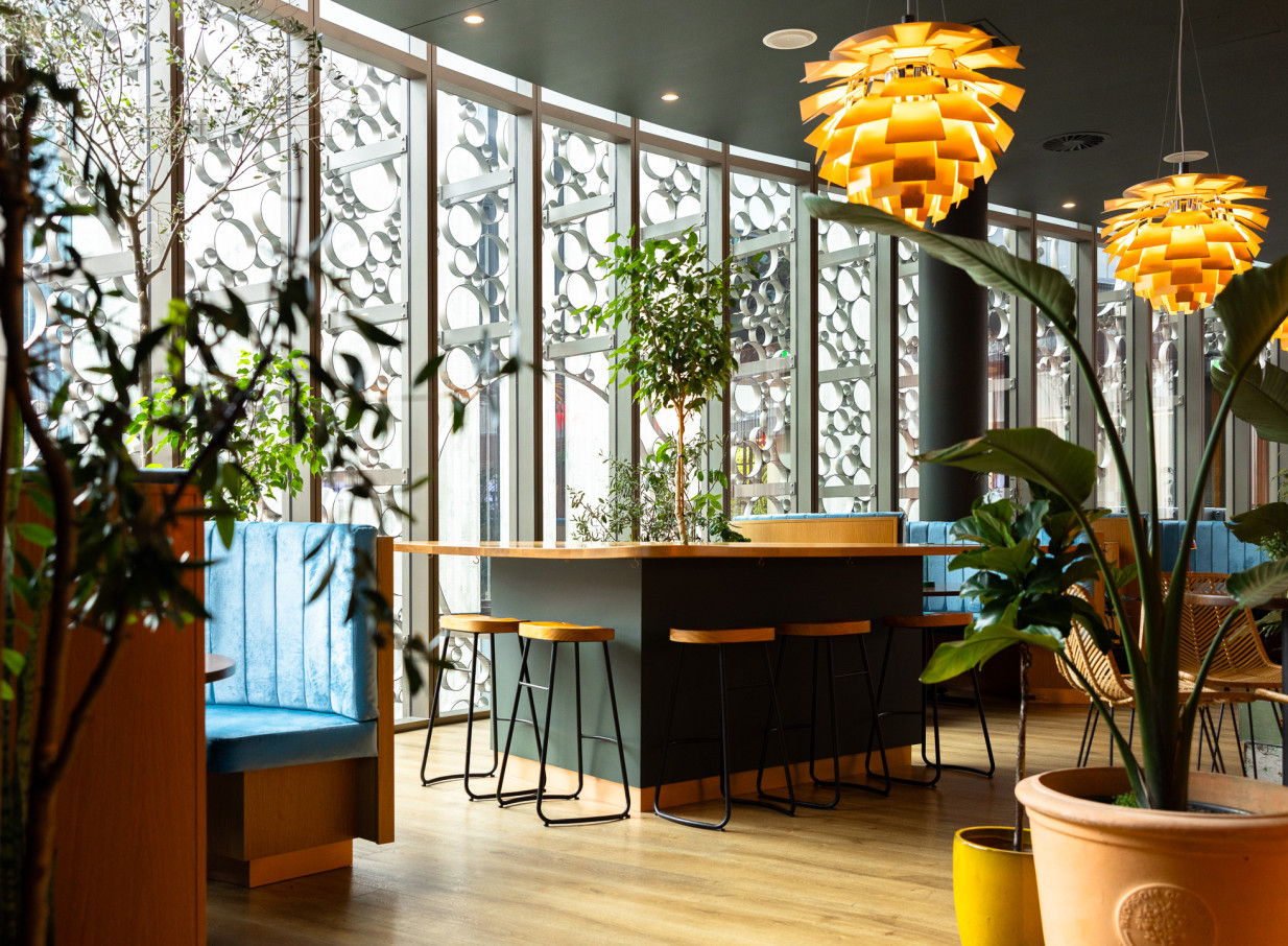 A vibrant modern Italian bar area at Bar Franco in Christchurch, featuring distinctive pendant lights, plush blue booths, and geometric window screens.